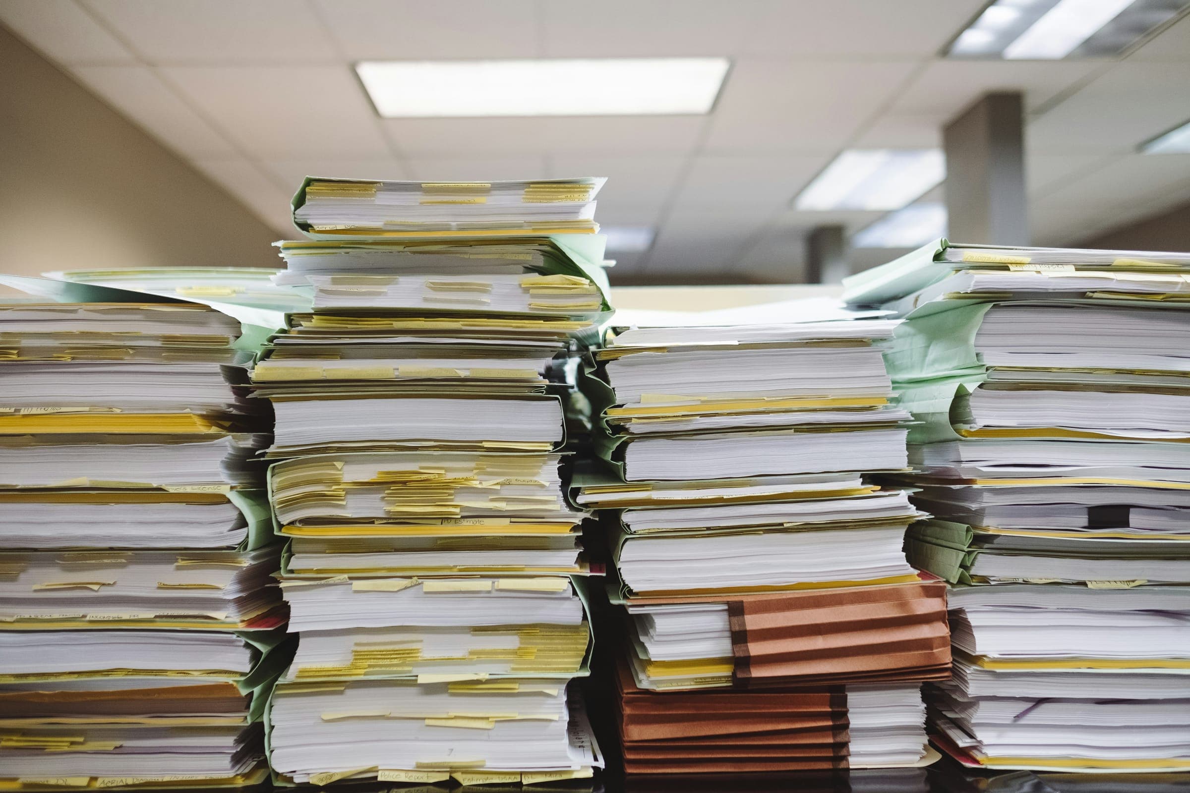 Pilas de expedientes y carpetas con documentos acumulados sobre un escritorio de oficina