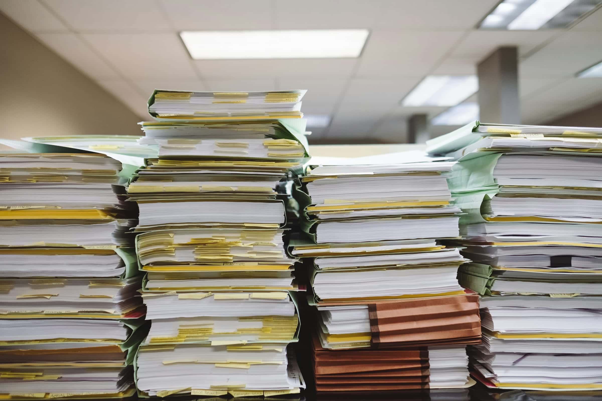 Pilas de expedientes y carpetas con documentos acumulados sobre un escritorio de oficina